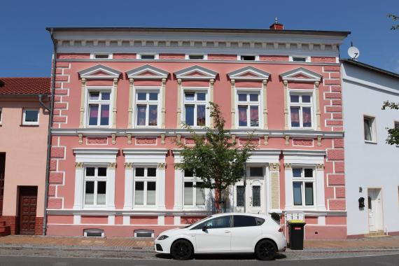 Frontal view of a house front. In the foreground a small car and a small tree