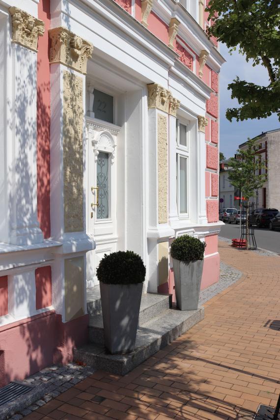 Eingangsbereich zu einem Haus, im Vordergrund zwei große Blumenkästen