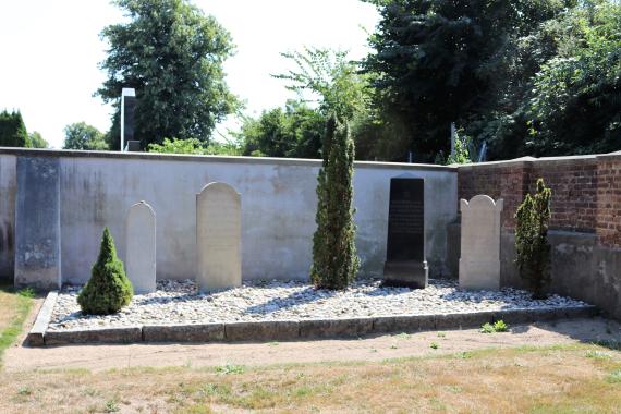 Jewish gravestones on a gravel bed. Behind it a wall.