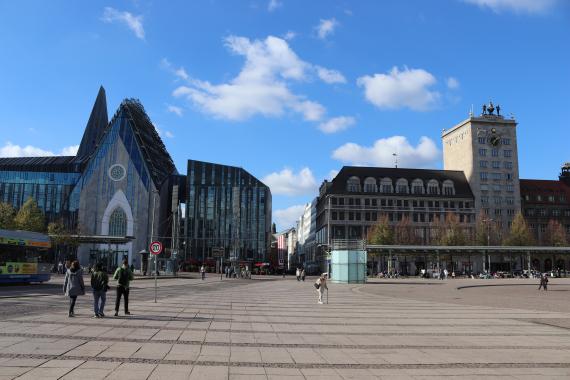 Large square. On the right, an older ensemble of buildings. On the left, a modern building made of steel and glass.