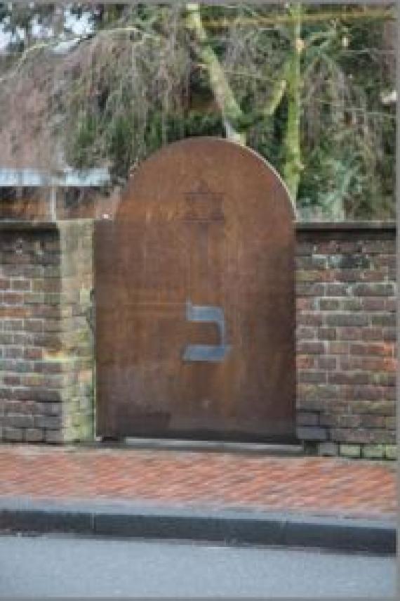 A gate with a wall. Supporting pillars. Hebrew characters on the gate.