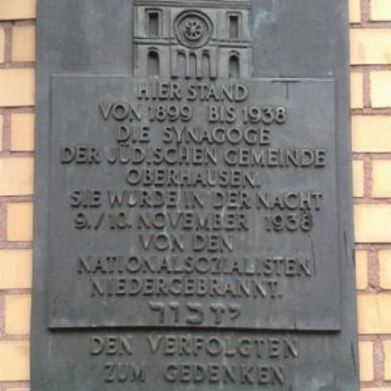 MMan sees a plaque made of bronze. The plaque commemorates the synagogue and its destruction by the Nazis