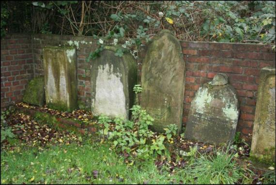 Some old gravestones. Weathered. They stand against the wall, not in their proper place.