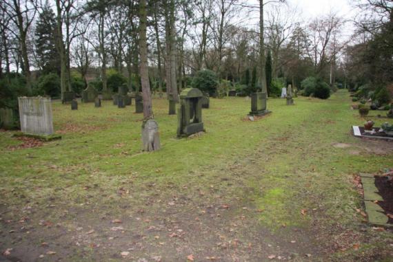 Several gravestones on a meadow. Behind them trees.