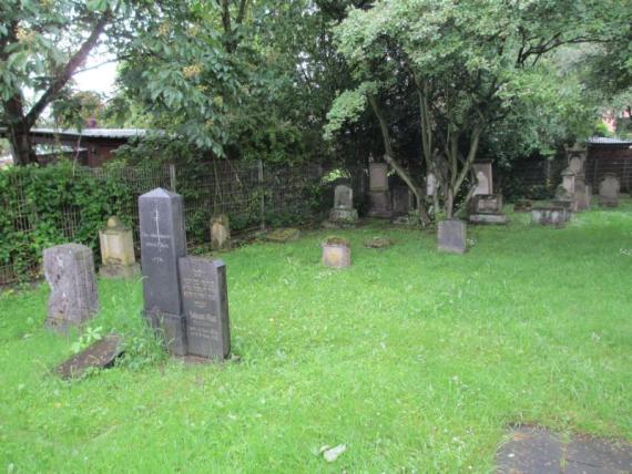 Some older gravestones on a meadow. The place is surrounded by trees and a fence.