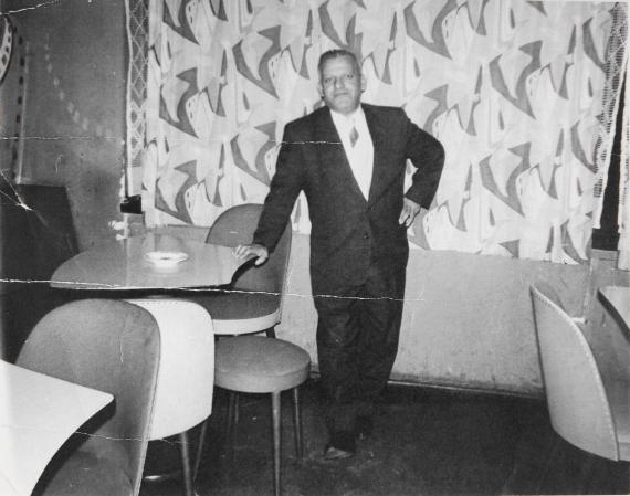 Samuel Steinfeld steht in seiner Bar Femina. Das Bild ist schwarz-weiß. Samuel trägt einen Anzug.