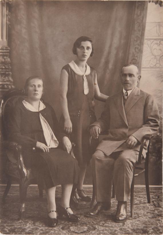 Israel and Miriam Steinfeld with their daughter. Black and white shot taken in photo studio. The parents are sitting. The daughter is standing in the middle.