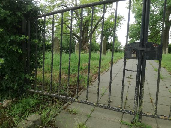 Blick durch das verschlossene Eingangstor - Blick auf Grabsteine auf der linken Seite