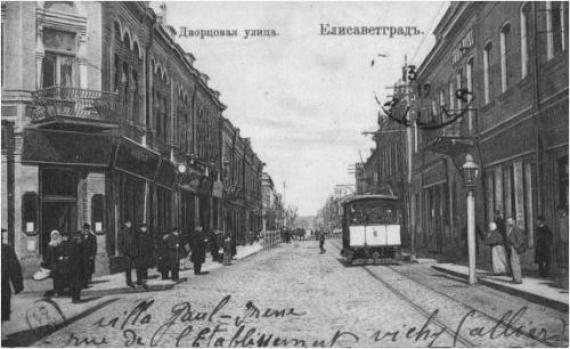 Old picture postcard with the view of the street. People walking on the left, a streetcar and tracks on the right.