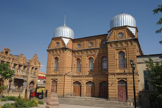 Der Blick von der gegenüberliegenden Straße auf das rot-orange Gebäude der Synagoge mit zwei silbernen Kuppeln.