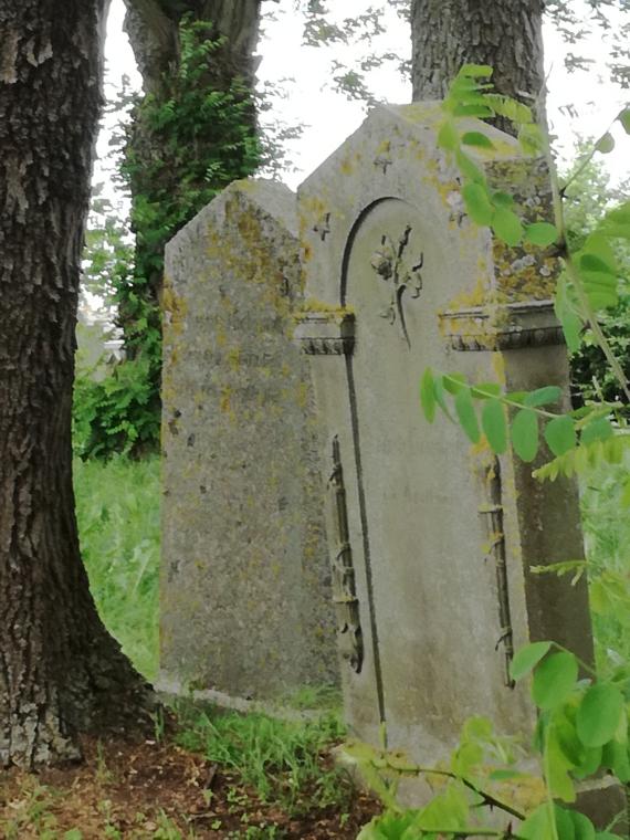 Close up of two gravestones to the right of the entrance behind a tree