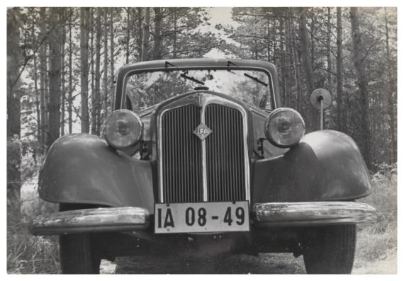 Schwarz-weiß-Foto, ein Auto wird von vorn gezeigt, es steht in einem Wald.