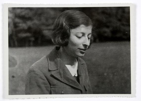 Fotografie in schwarz-weiß, auf welchem die jugendliche Helene zu sehen ist. Es ist eine Nahaufnahme, auf welchem sie nach unten blickend leicht lächelnd vor einem Wald zu sehen ist.