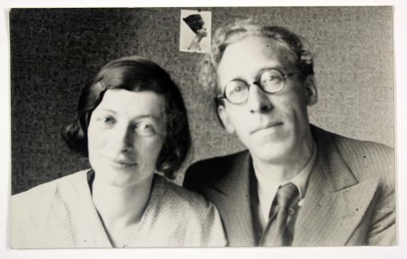 Schwarz-weiß Fotografie, auf welchem ein junges Paar sitzend vor einer Wand zu sehen ist. Sie lächeln freundlich.