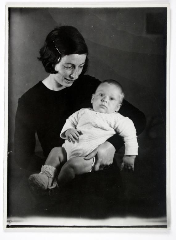 Schwarz-weiß Fotografie, auf welchem eine junge, schlanke Frau mit dunklen Haaren zu sehen ist, welche ein pummeliges Baby im Arm hält. Sie blickt lächelnd auf das Baby hinab.