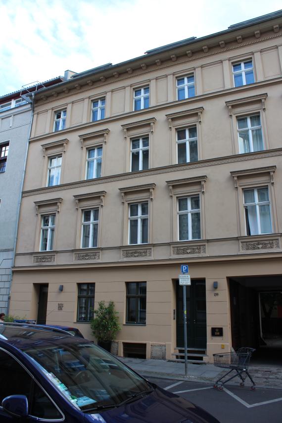 Frontansicht auf ein beiges vierstöckiges Haus. Unter den Fenstern im 1. Stock befindet sich verspielter Stuck.