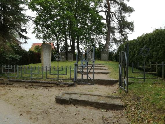 Eingangsor und Zaun mit Blick auf den Gedenkstein links und die Gräber