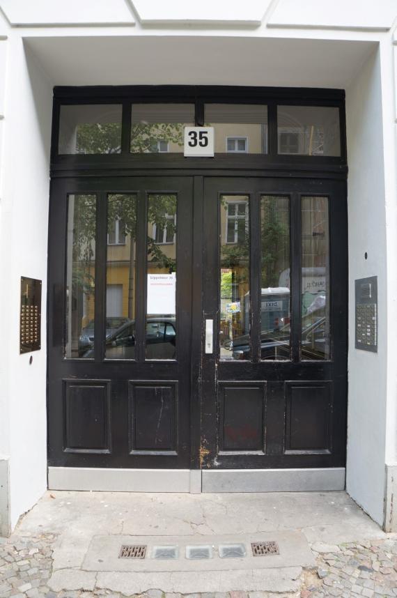 Black lacquered front door with glass panes, in the door reveal on the left the memorial plaque and opposite on the right the bell system of the current occupants of the house.