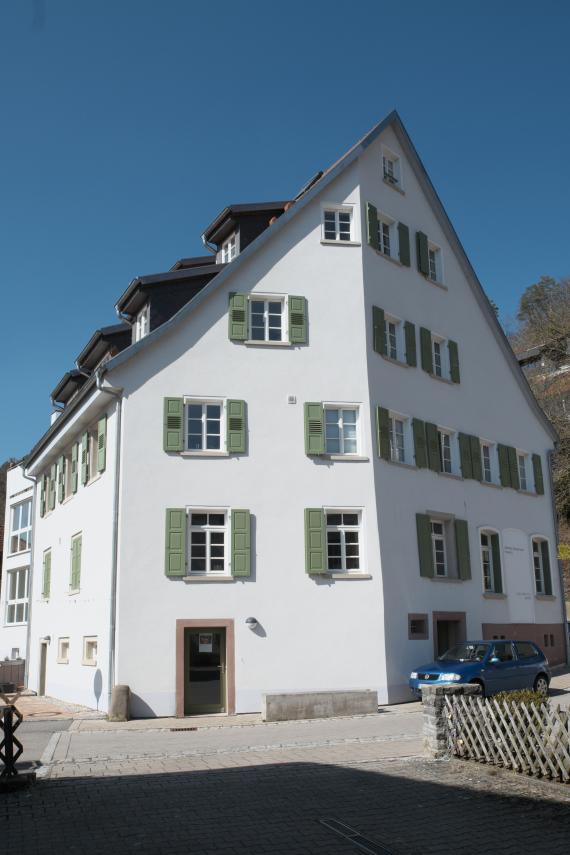 Zu sehen ist eine Farbfotografie eines weißen Hauses mit Schrägdach, in der sich der ehemalige Betsaal befand.