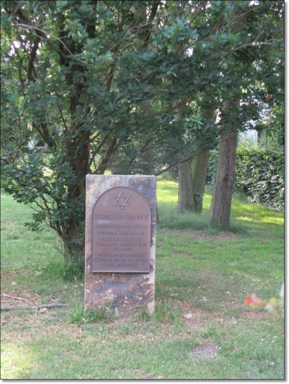 Gedenkstein auf dem Friedhof, im Hintergrund sind einige Bäume zu erkennen.