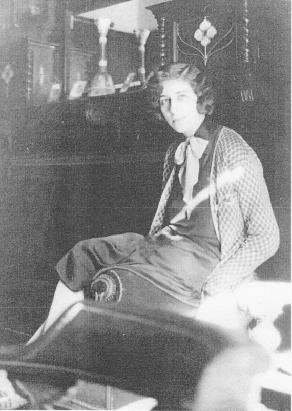 Hildegard Lewy, the elder daughter of Lina and Isidor Lewy, sits on a sofa back in front of an ornate cabinet or buffet in the family apartment Vorderhaus 2.OG.