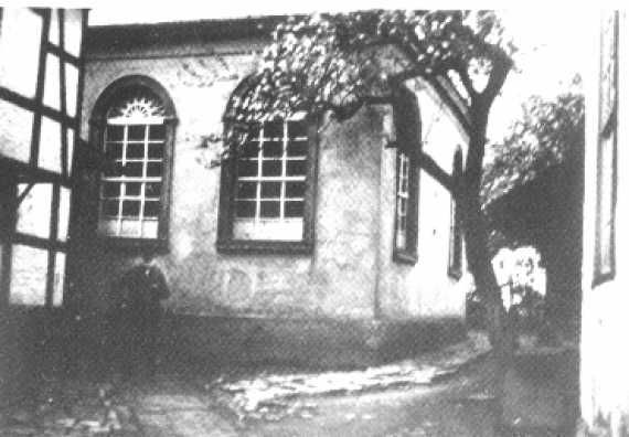 Teil der Fassade der ehemaligen Synagoge in Werther, im Vordergrund ein Baum und ein Fachwerkhaus.