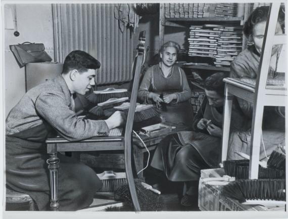 Three women and one man in the workshop of the Jewish Workshop for the Blind in Germany: the man and one woman are tying the weave of a chair, the other two women are making brushes.  The photo is retouched.  It is the Jewish Institute for the Blind for Germany e.V. in Berlin-Steglitz.Jewish Workshop for the Blind for Germany: the man and a woman are tying the weave of a chair, the other two women are making brushes.