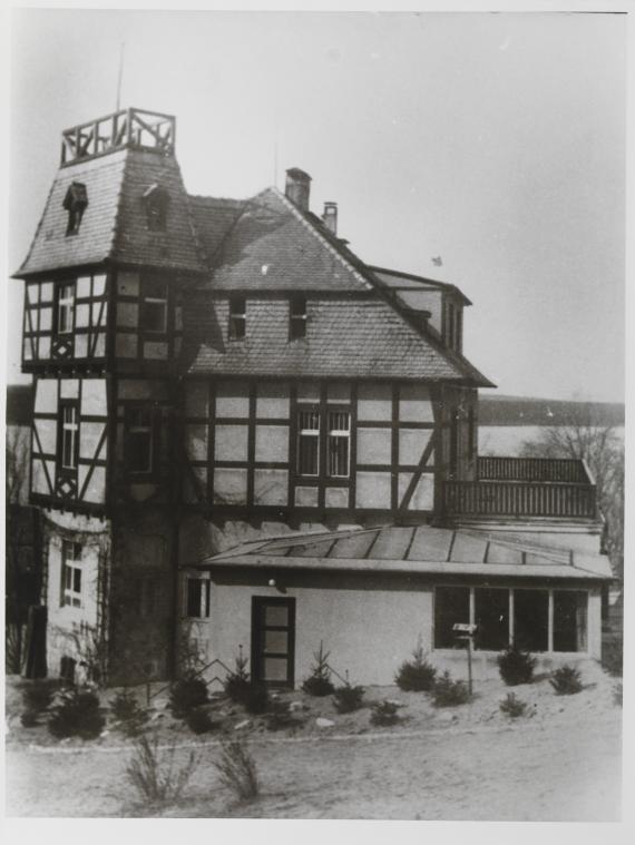 You can see the main house. There are windows. In front of the house are also bushes that fence the house.