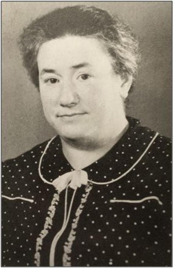 Schwarz-Weiß Portrait von Martha Landsberg, geb. Cohnheim. Sie trägt ein dunkles Kleid mit hellen Punkten, es ist mit Rüschen und einer kleinen Schluppe verziert. Sie befindet sich in ihren Mittvierzigern.