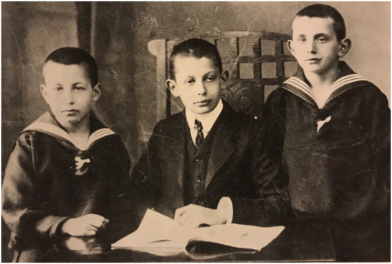 The picture shows the dark-clad brothers Bruno, Julius and Max Wallheimer in their older childhood behind a table.