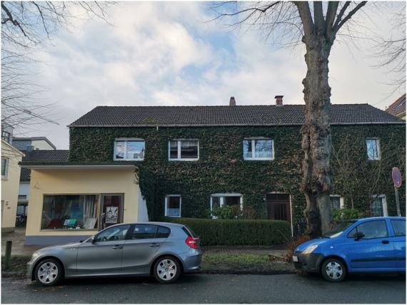 Aktuelle Farbfotografie des ehemaligen Wohnhauses Tahls. Das Bild zeigt ein von Efeu überwachsenes Haupthaus sowie links einen kleinen Anbau mit gelber Fassade. Durch dessen Schaufenster sind einige Bilder und Malereien zu sehen. In letzterem befand sich Gustav Tahls erstes Tageslichtatelier.