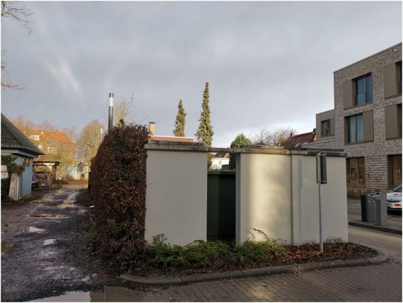 Current photo of the former second photo shop Tahls in Bremer Street. The picture shows a small wall complex framed by a hedge and some plants. To the right and left of it are adjacent residential buildings.