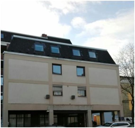 Farbfoto vom ehemaligen Standort des Gebäudes der Firma „M.L. Reyersbach A.G.“ Es handelt sich heute um ein Wohnhaus. Zu sehen ist ein breites Gebäude, welches über vier Etagen verfügt. Unten befindet sich eine ladenähnliche Konstruktion mit vielen Glasfenstern, welche durch den Überbau des Hauses überdacht ist.