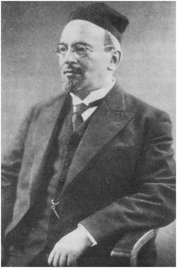 Black and white photo of Dr. phil. Philipp de Haas. In it, de Haas is sitting on a wooden chair, with only his upper body visible. The picture itself was taken from the front, while de Haas is looking to his right. He is wearing a dark suit and glasses without frames.