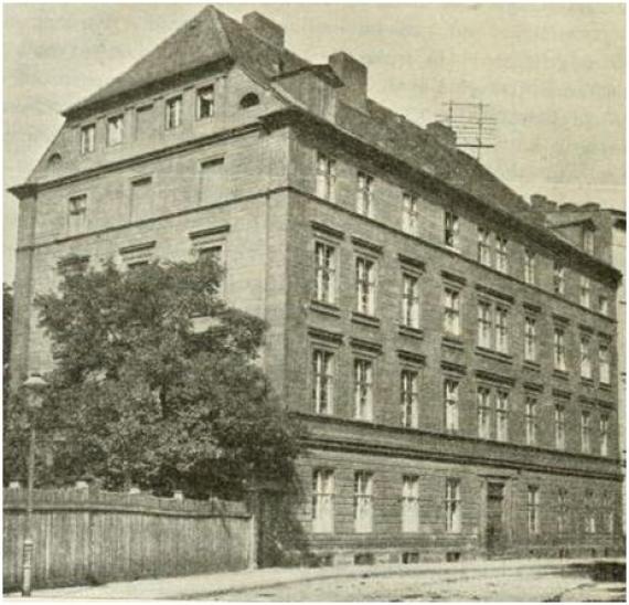 The picture shows the Jewish Theological Seminary in Wroclaw. The building is shown in black and white and can be seen slightly from the side. Also visible is the street on which the building is located, as well as a large tree that covers a side wall.