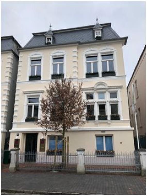 The picture shows the front view of the building of Moltkestraße 6a in Oldenburg. In addition to the first floor, the house consists of two other floors and a smaller attic. In front of the house there is a tree reaching up to the second floor. The property is bordered by a fence.