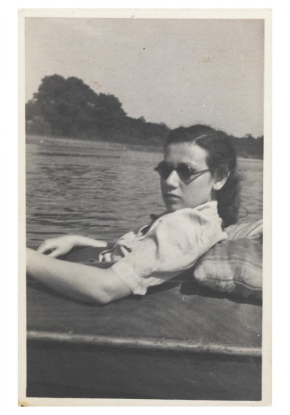 Portrait of Felice Schragenheim sitting reclined in a boat. She wears sunglasses and looks into the camera in three-quarter profile. In the background, a lake and plantings on the other shore can be seen.