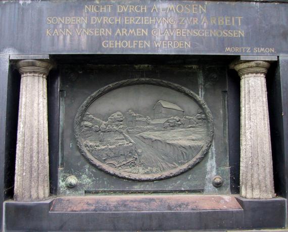 Grabmal von Moritz Simon (1837-1905), Gründer der Israelitischen Gartenbauschule Ahlem, auf dem jüdischen Friedhof An der Strangriede Oben das Lebensmotto Simons zur Berufsumschichtung der Juden, darunter zwischen zwei Säulen im Bronzemedaillon eine stilisierte Abbildung der Israelitischen Gartenbauschule Ahlem mit Getreidefeld, Pflug, Bienenhaus, Eingangstor, Gewächshäusern und Hauptgebäude.