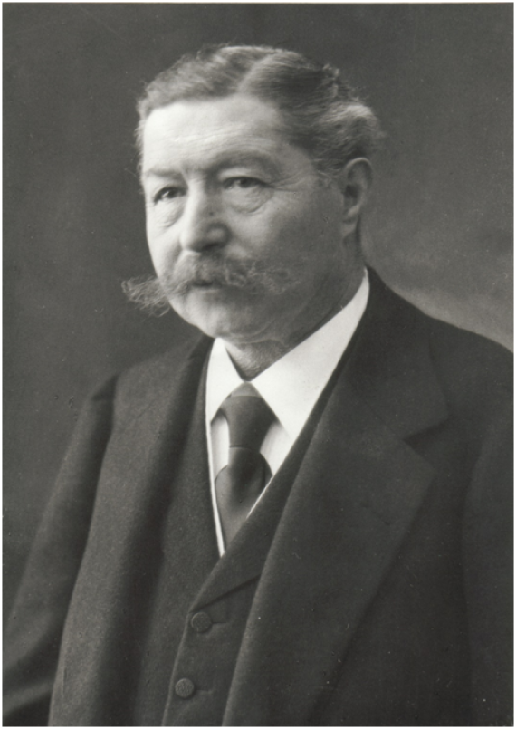 Portrait photo of Gustav Strupp. He wears a tie, vest and suit, a side parting and has a bushy, protruding mustache