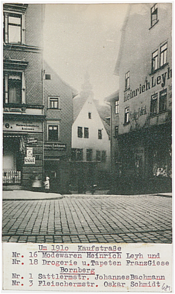 Die Kaufstraße um das Jahr 1910. Die Fotographie zeigt Häuser, die Straße sowie ein kleines Kind und um Hintergrund einen Kirchturm. 