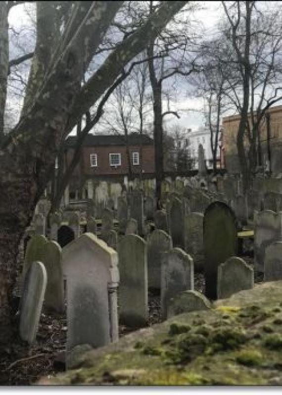 A wall. Behind it individual gravestones.