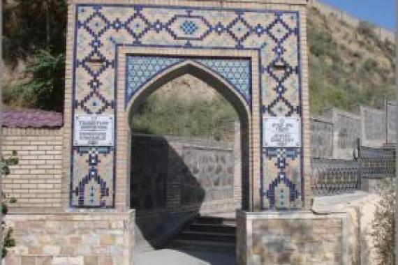 A colorful clinkered large gate. Behind it a staircase leading to the right up a stony hill. Bright sunlight.