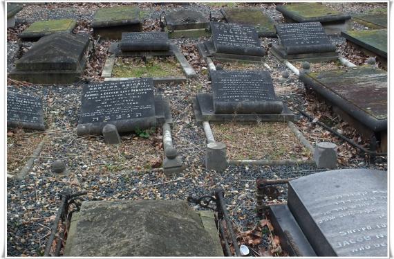 Closely arranged grave slabs on uneven gravel surface