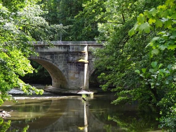 Ausschnitt einer alten Steinbrücke, die über einen Fluss führt. 