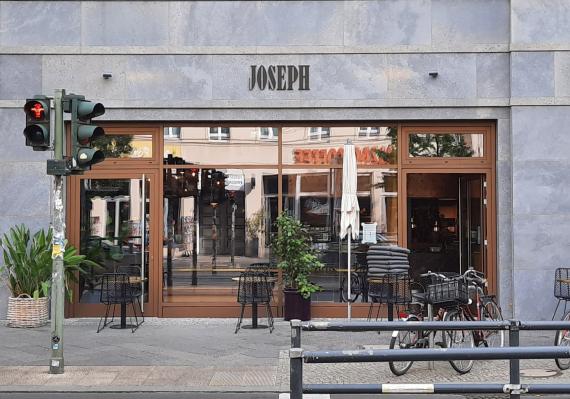 A cafe with a high window front. In front of it are tables and chairs.