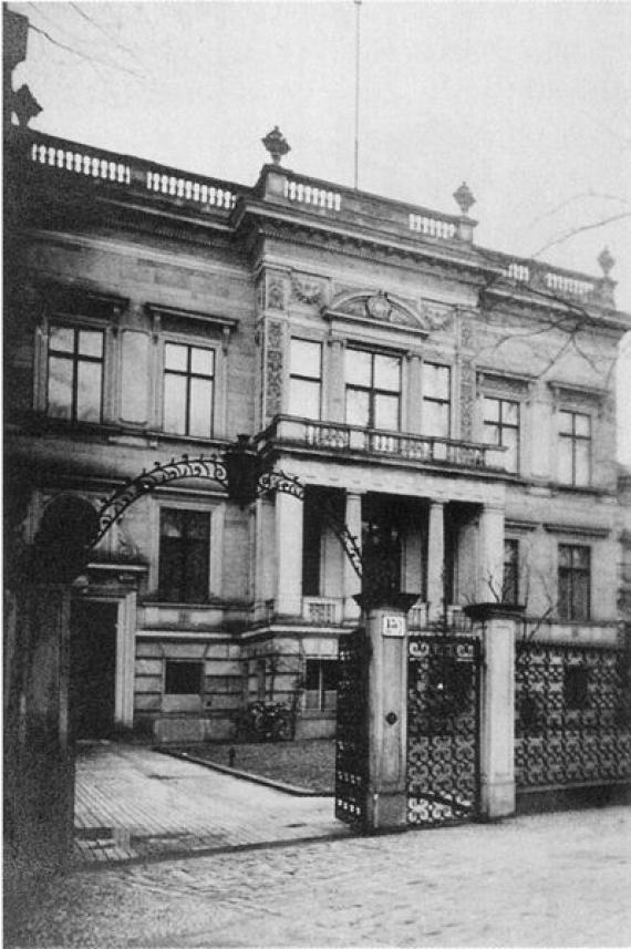 Black and white picture with big building. In front of it garden, fence and gate.