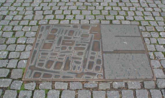 Metallplatte auf dem Boden. Alter Stadtplan und Informationstext sind abgebildet.