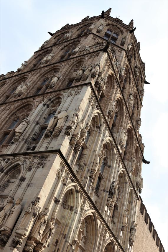 Aufnahme eines alten Turms aus der Froschperspektive. Das Gebäude hat viele Verzierungen und Fenster.