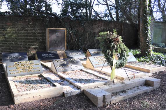 Picture of a grave site. Several gravestones are lined up and a funeral wreath stands in front of it....