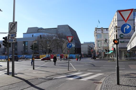 Heutiges Foto der Kölner Glockengasse. Moderne Häuser, Ampeln und eine Straße sind abgebildet.